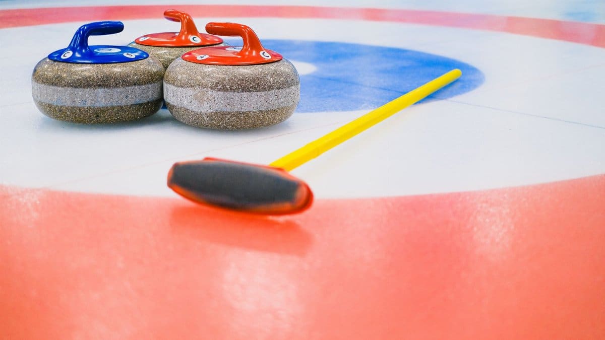 Heavy granite curling stones with handles and broom placed on ice in colorful circular target area during game in arena