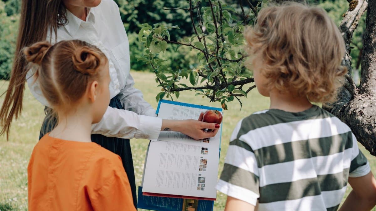 A woman teaching children about apples in a garden, engaging in outdoor education.