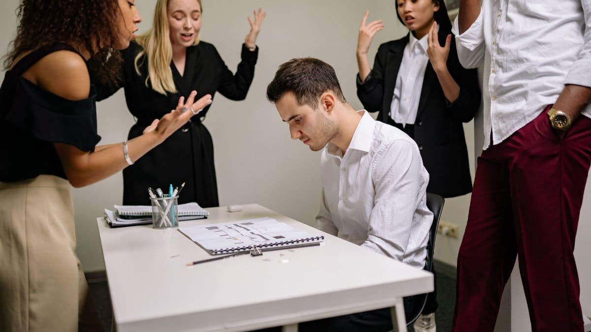 A team confronts a stressed colleague at a tense office meeting, highlighting workplace dynamics.