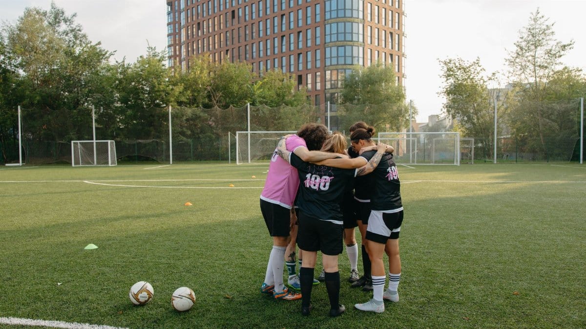 Female soccer players in a huddle on a grass soccer field, preparing for a match.