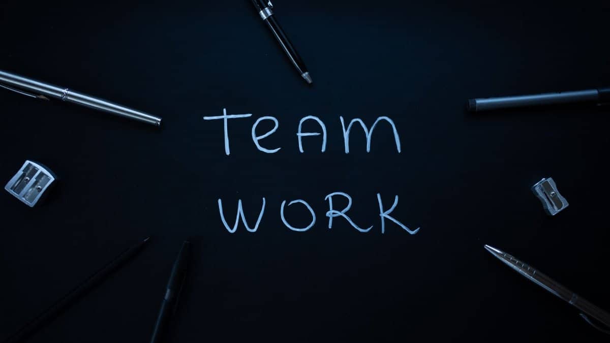 Arrangement of office supplies around teamwork text on black background.