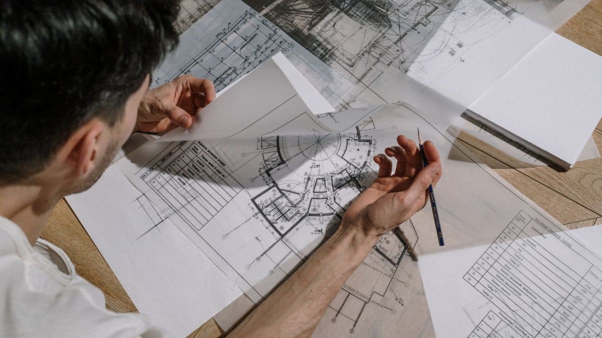 Architect studying and sketching over detailed architectural blueprints indoors.