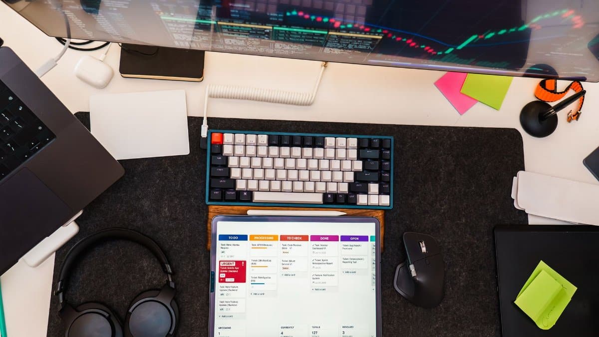 Top view of a tech workspace featuring a digital tablet, keyboard, monitor, and headphones for project management.