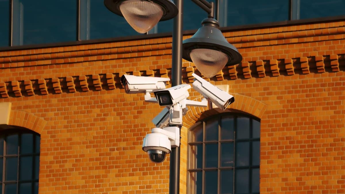 Modern security cameras mounted on a pole against a brick building in the city.