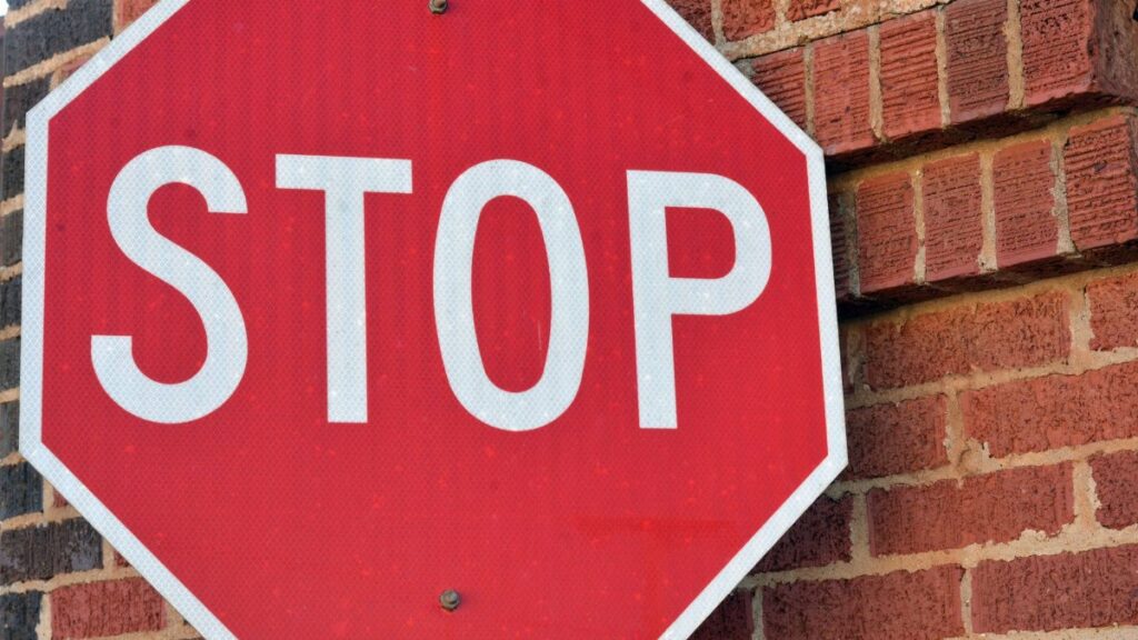 Red stop sign mounted on a brick wall in Henderson, Texas, during the day.