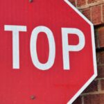 Red stop sign mounted on a brick wall in Henderson, Texas, during the day.