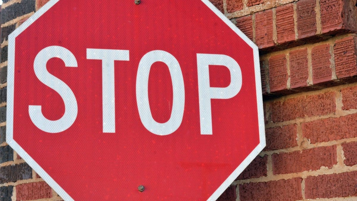 Red stop sign mounted on a brick wall in Henderson, Texas, during the day.