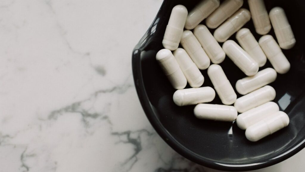 Close-up of white capsules in a black bowl on a marble surface, symbolizing healthcare and medication.