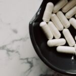 Close-up of white capsules in a black bowl on a marble surface, symbolizing healthcare and medication.