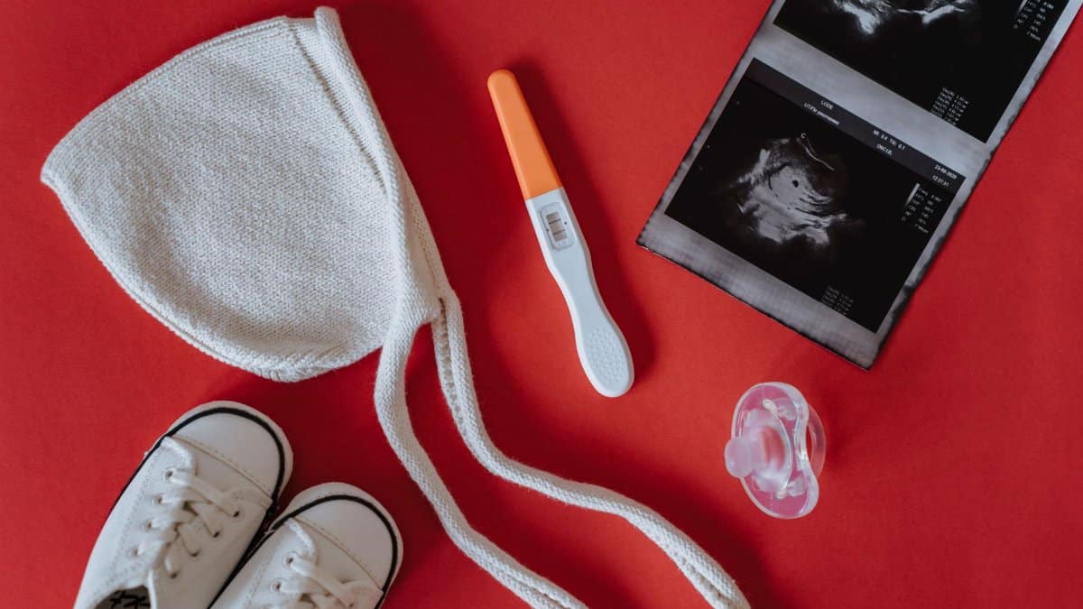 Flat lay of pregnancy announcement with baby items on a red background.
