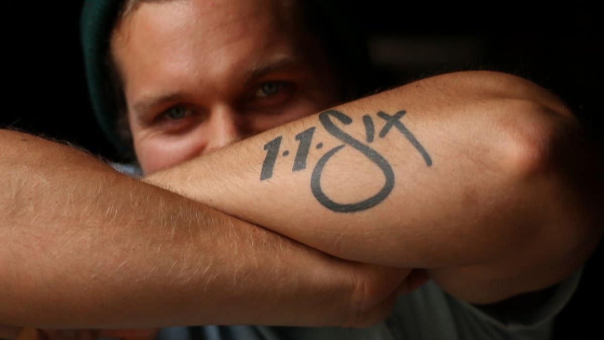 Close-up of a young man smiling, showing off his arm tattoo with vivid expression.