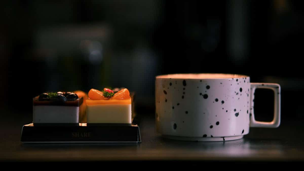 Stylish speckled coffee mug alongside gourmet desserts in dimly lit setting.