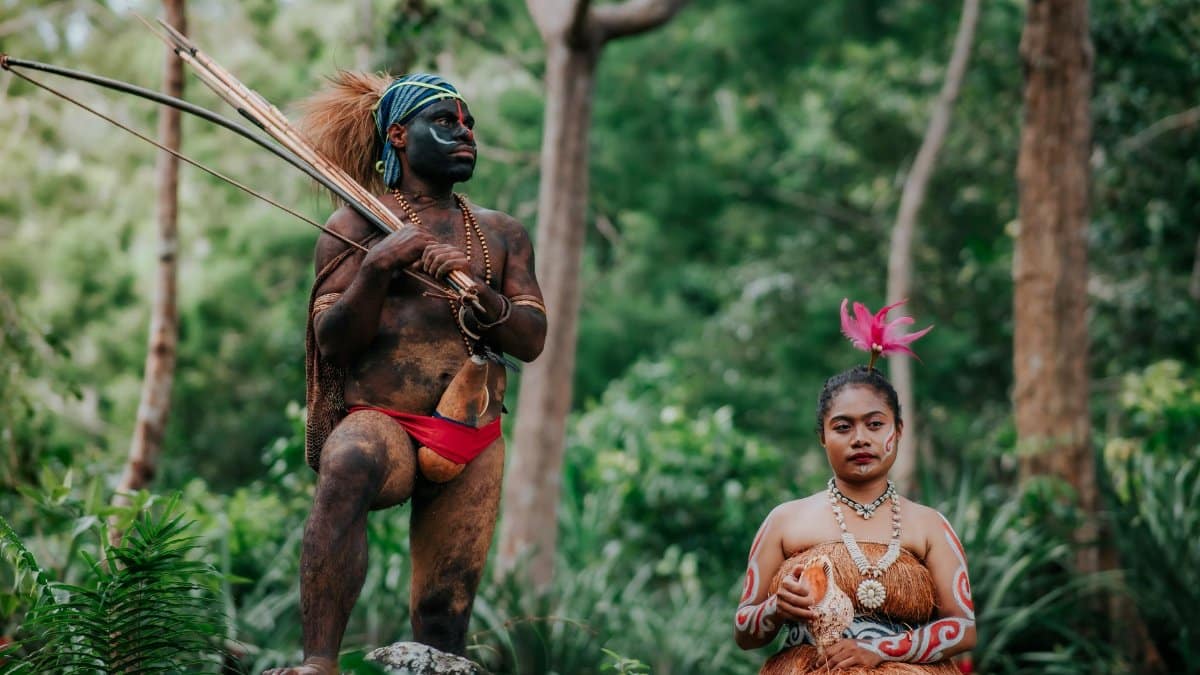 Two individuals in traditional tribal attire in a lush forest environment.
