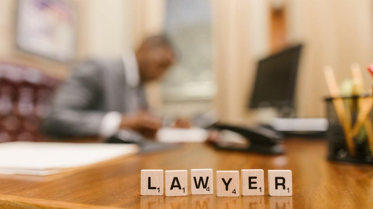 Wooden letter tiles spelling 'LAWYER' on a desk, with blurred office setting in the background.