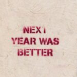 Rustic wall art with an inspirational message 'NEXT YEAR WAS BETTER' stenciled on a textured surface.