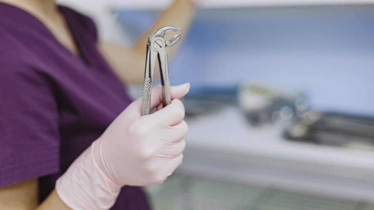 Close-up of a dentist's hand holding extraction forceps in a sterile dental clinic environment.