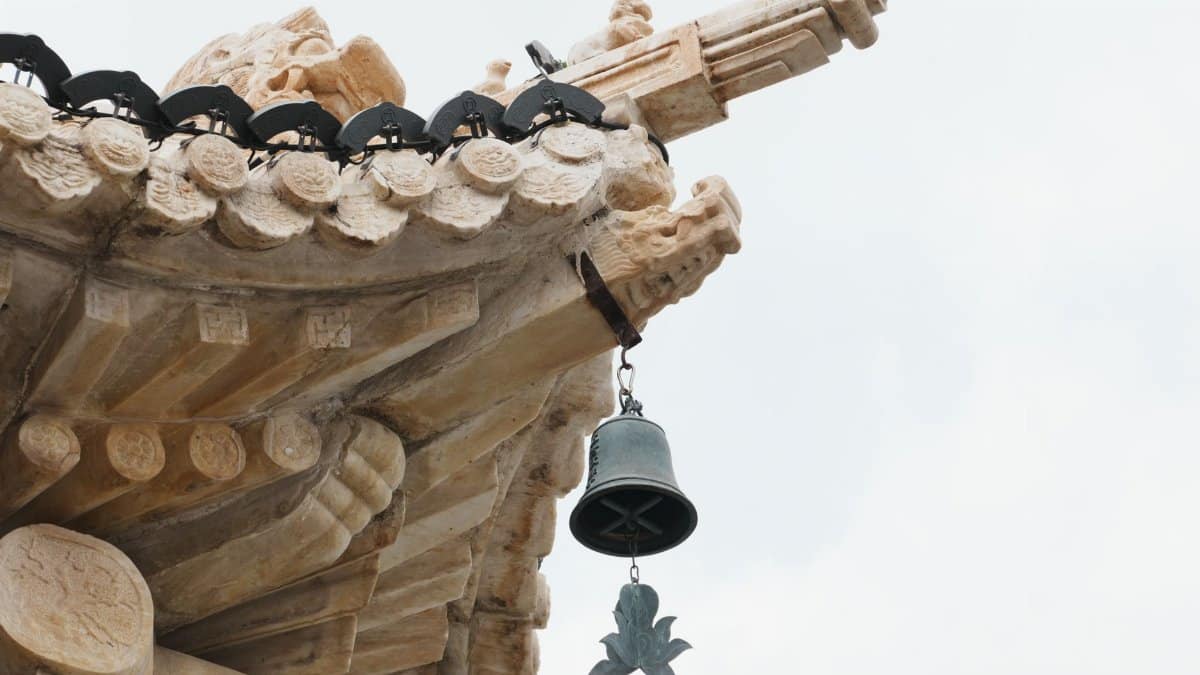 Close-up of a traditional temple roof ornament and bell, showcasing intricate Asian architectural details.