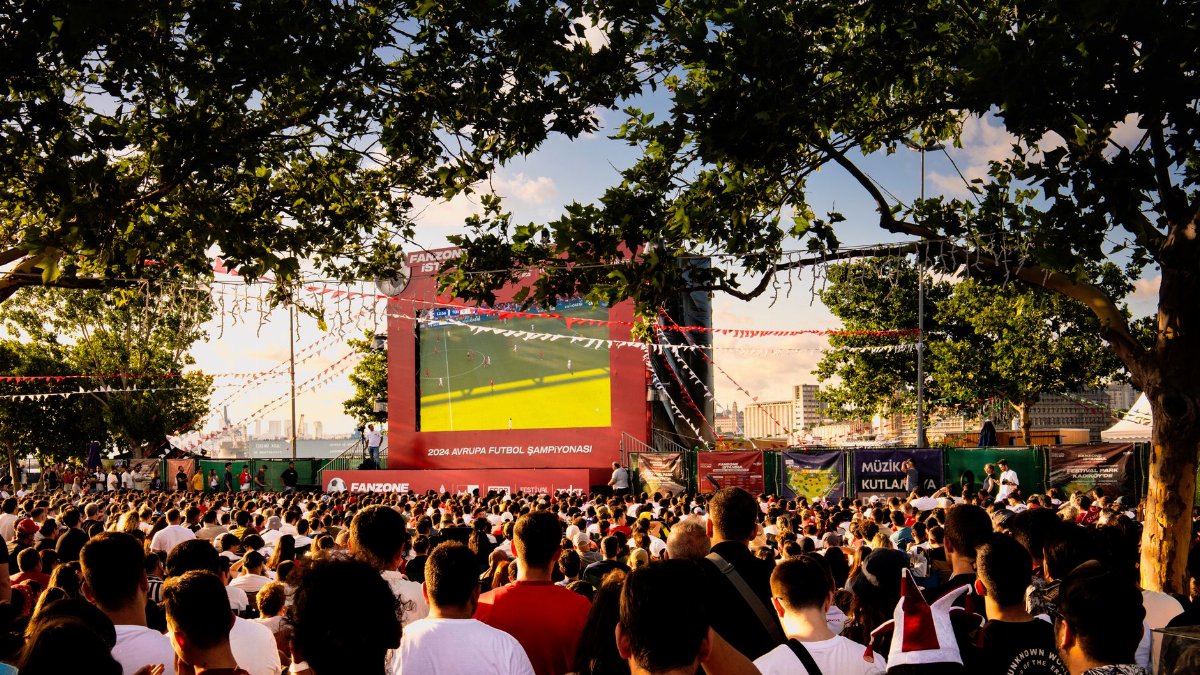 Crowd gathered in İstanbul park watching Euro football on big screen. Energetic summer atmosphere.