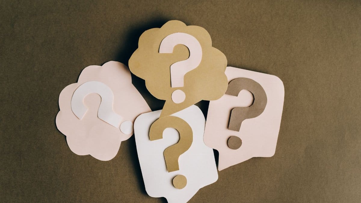 Four paper cutouts of question marks in beige and white on a brown surface, symbolizing inquiry and curiosity.