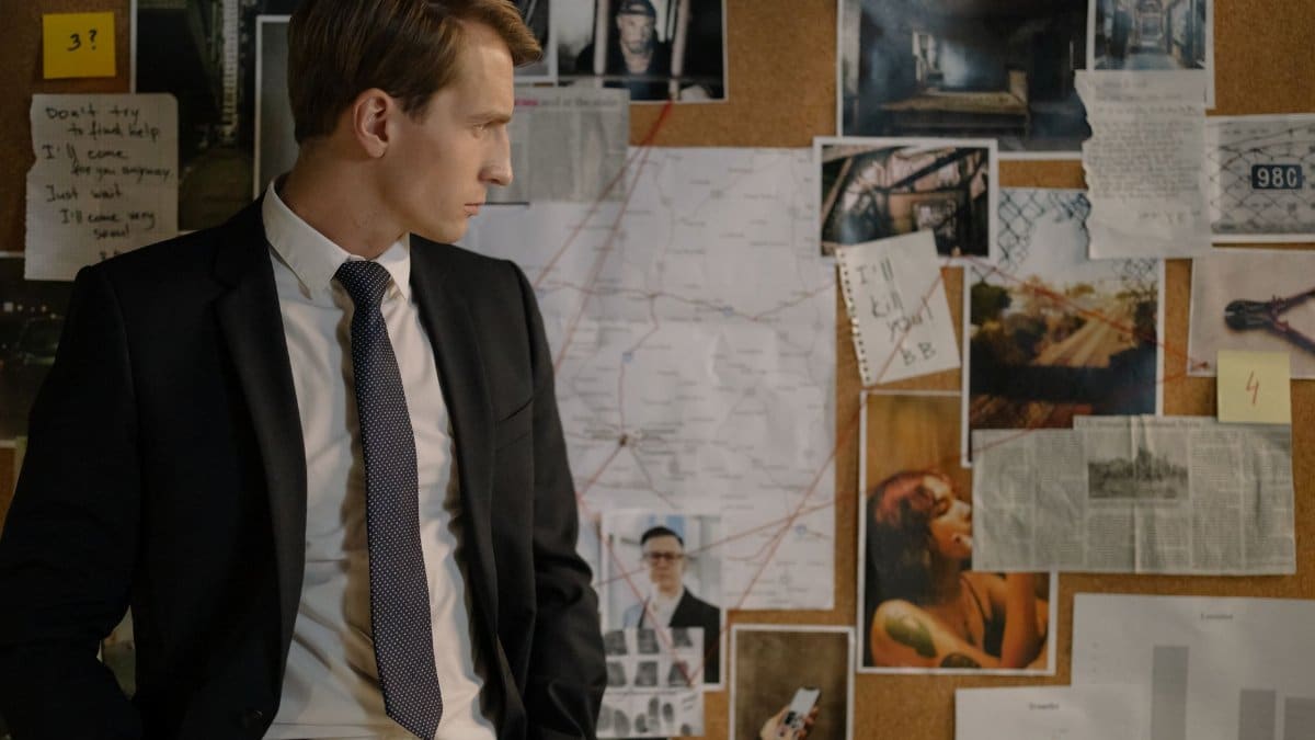Detective in suit examining evidence on cork board during investigation process.