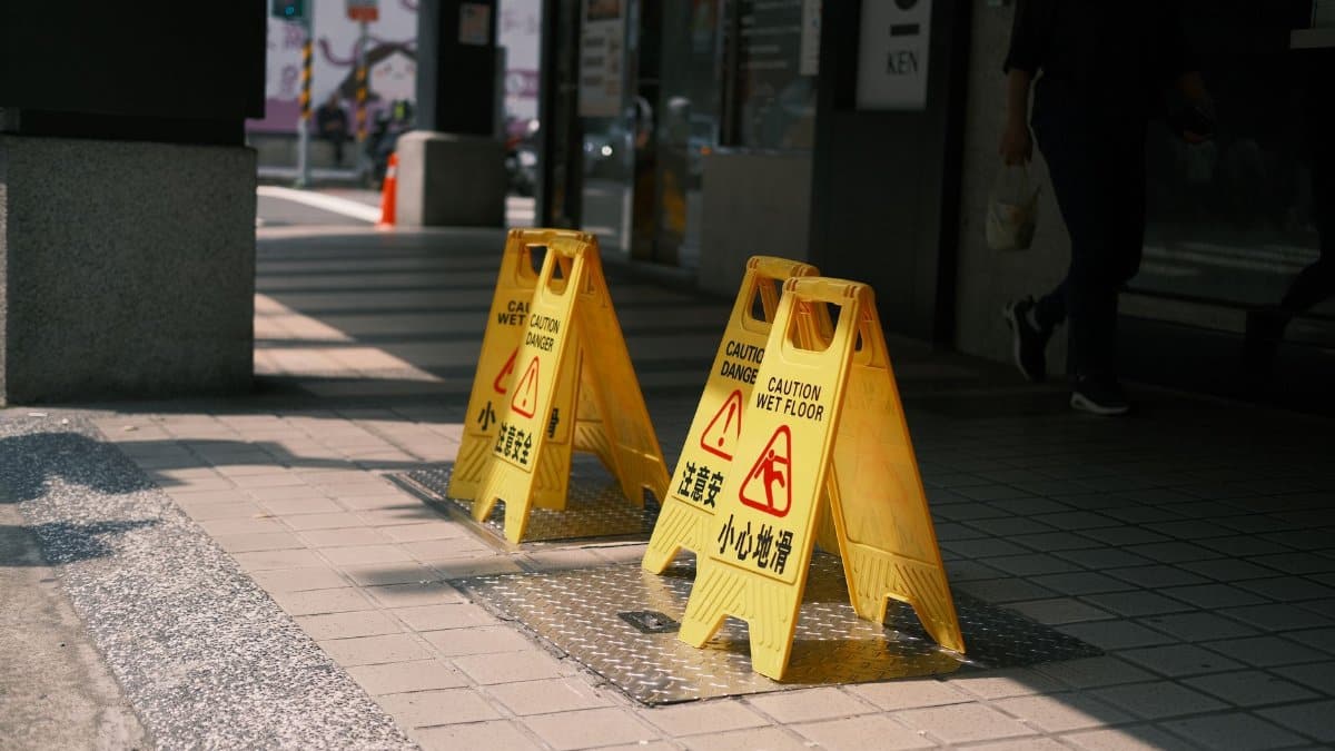 Yellow caution wet floor signs on a sunlit outdoor sidewalk, indicating a safety warning.