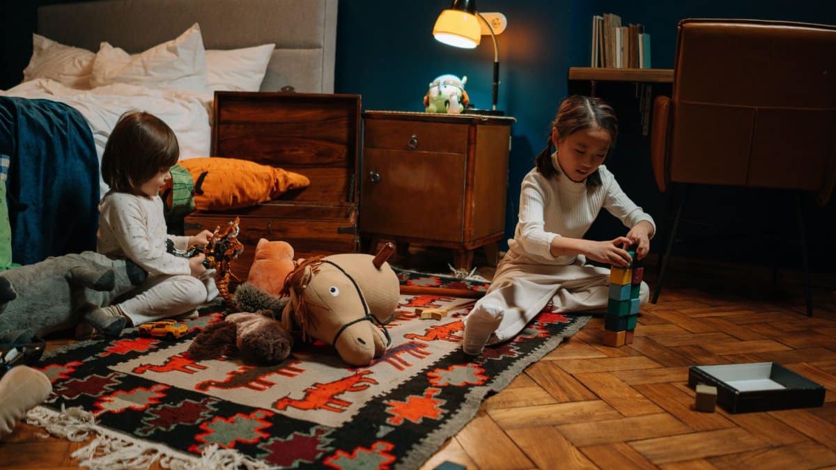 Two children in pajamas play with toys in a warmly lit bedroom, creating a joyful scene.