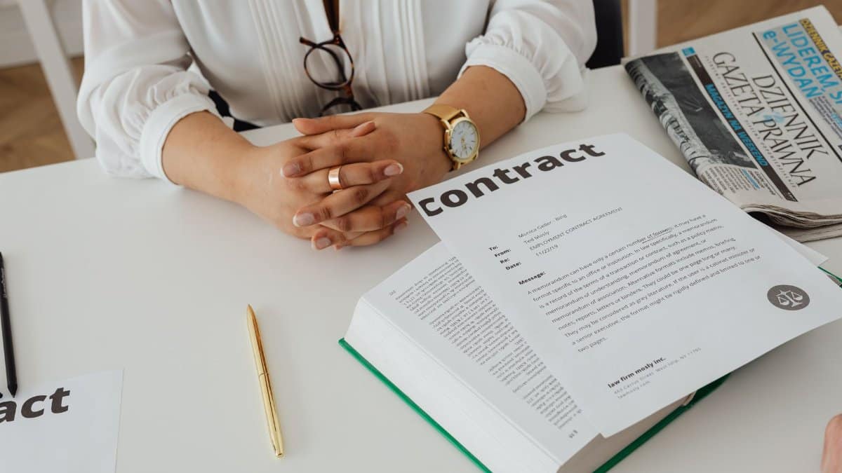 Businesswoman sitting at desk reviewing contract with legal documents and newspaper.