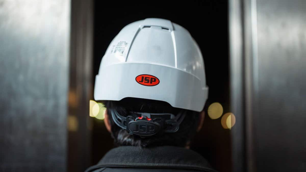 Close-up of an industrial worker wearing a JSP safety helmet at night, viewed from behind.