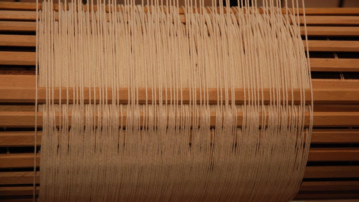 Detailed view of a wooden loom in action with yarn threads, highlighting traditional weaving techniques.