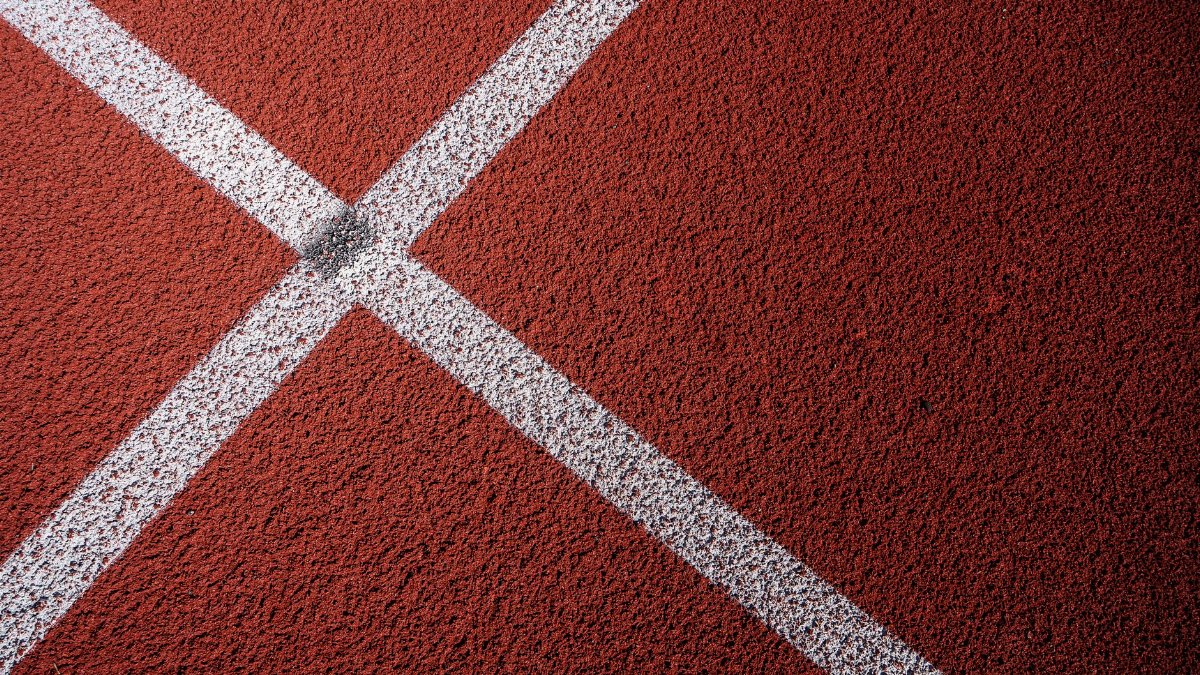 Detailed view of a red sports track surface featuring intersecting white lines, ideal for texture backgrounds.