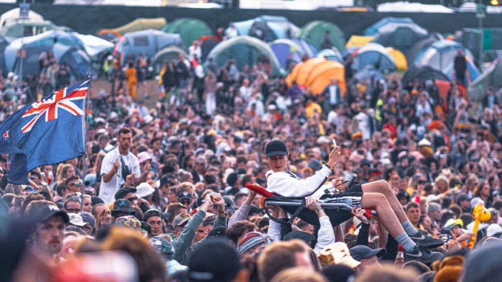 Exciting scene of a crowd surfing at an outdoor music festival with camping tents.