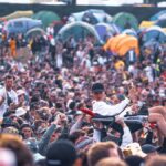 Exciting scene of a crowd surfing at an outdoor music festival with camping tents.