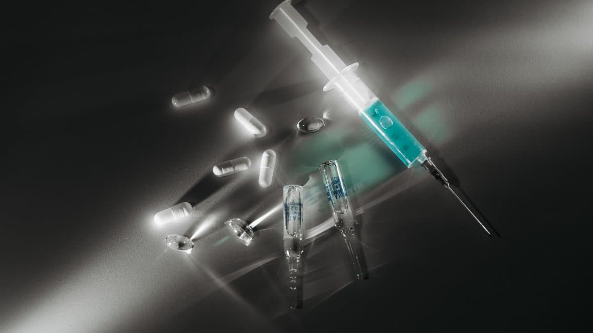 Syringe and medicine capsules illuminated in a dark, dramatic setting, emphasizing medical themes.