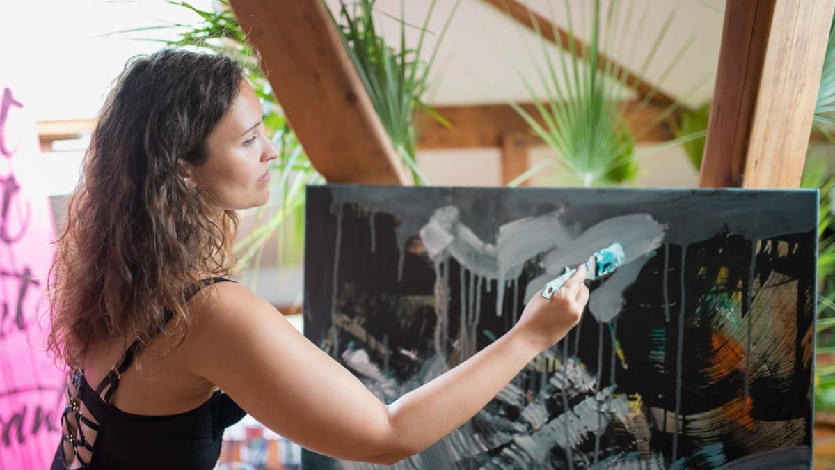 A woman artist passionately paints an abstract artwork on canvas in a vibrant studio.