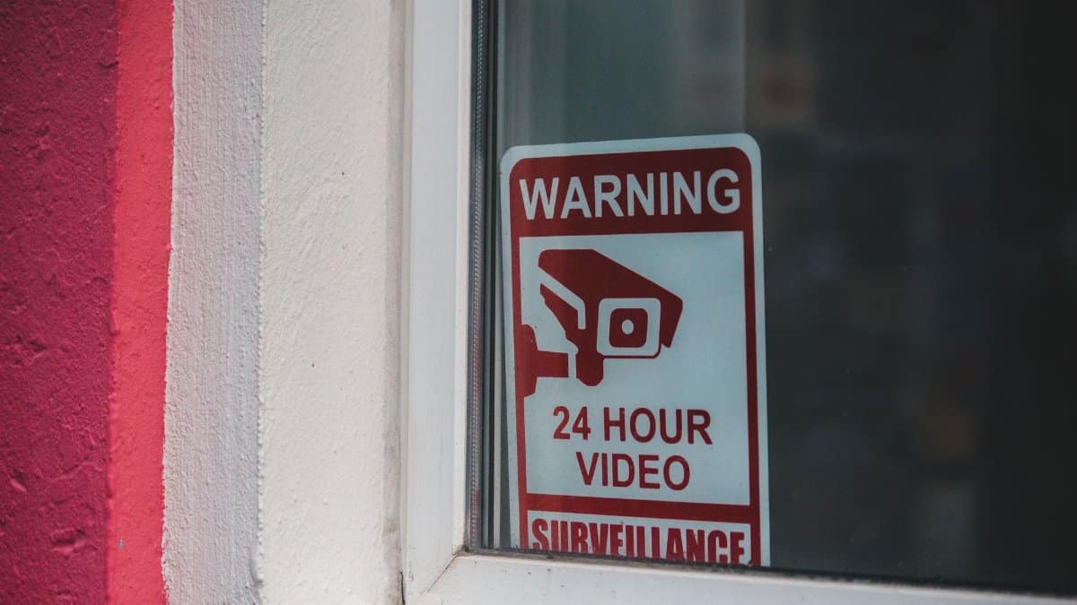 Red warning sign of video surveillance placed behind window of building in daytime