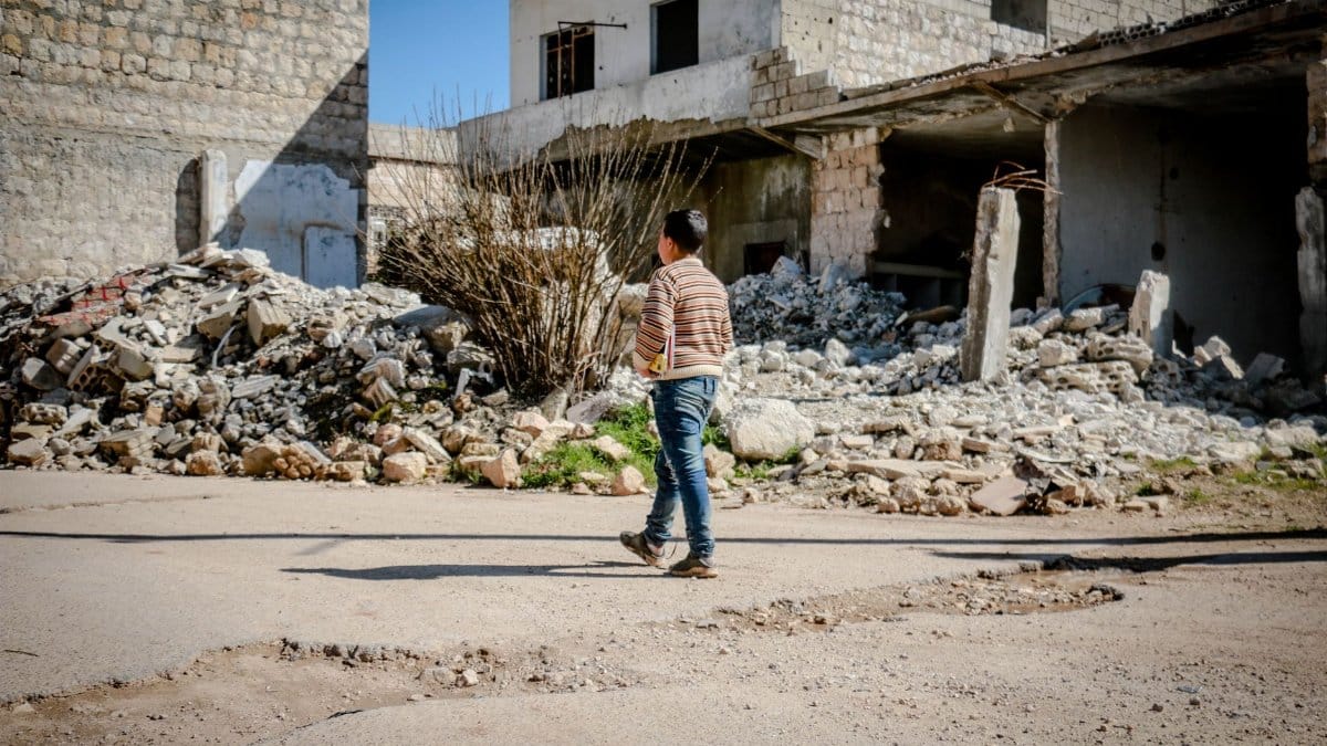 A young boy walking past rubble in a conflict-affected area of Idlib, Syria.