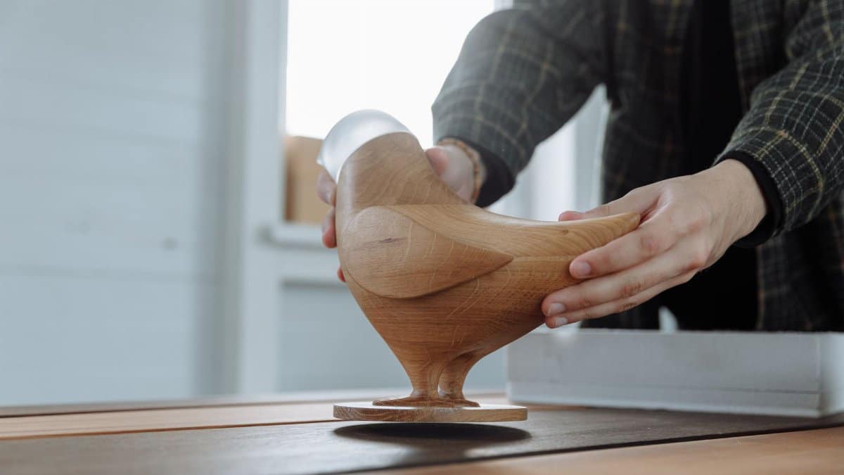 Close-up of hands carefully holding a handmade wooden bird sculpture, showcasing artisan craftsmanship and design.