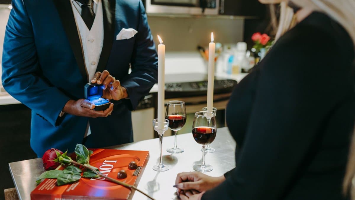 A romantic proposal with a man presenting a ring to a woman over wine and candlelight.