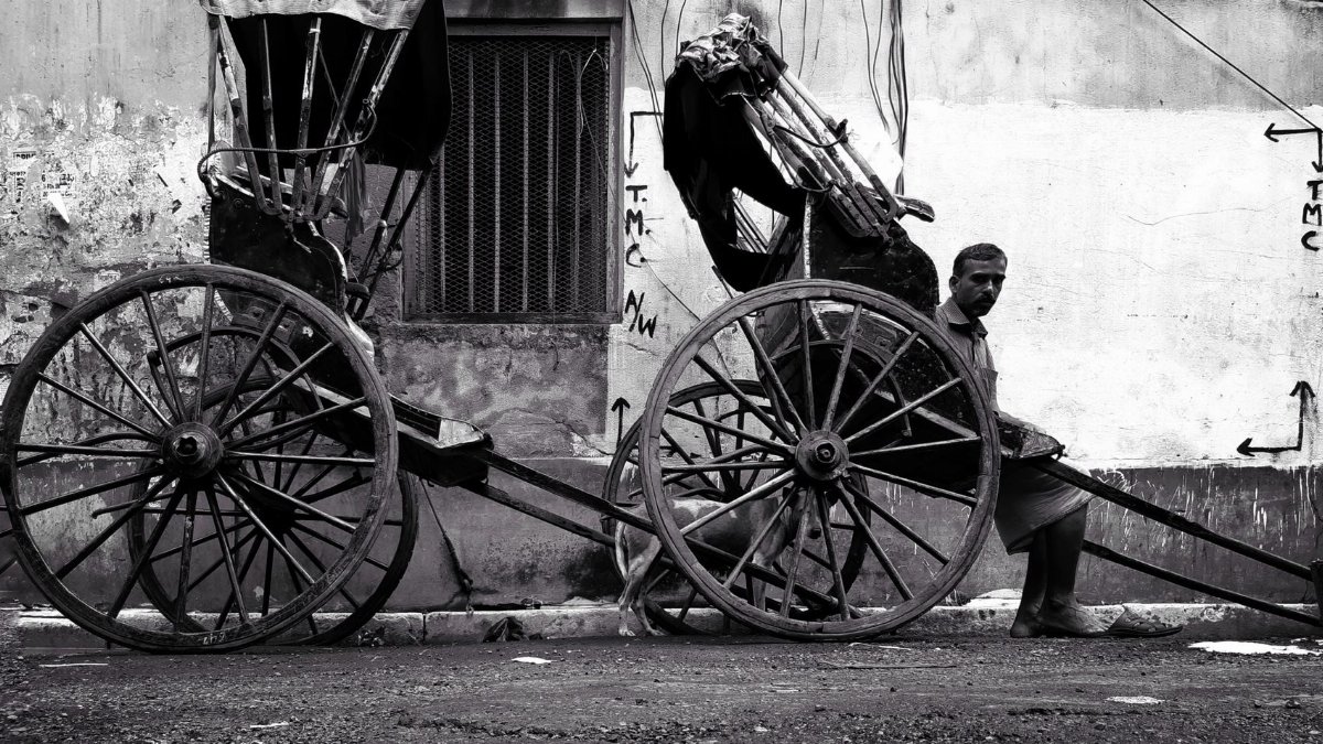 Black and white photo of a rickshaw puller and cart on a Kolkata street.