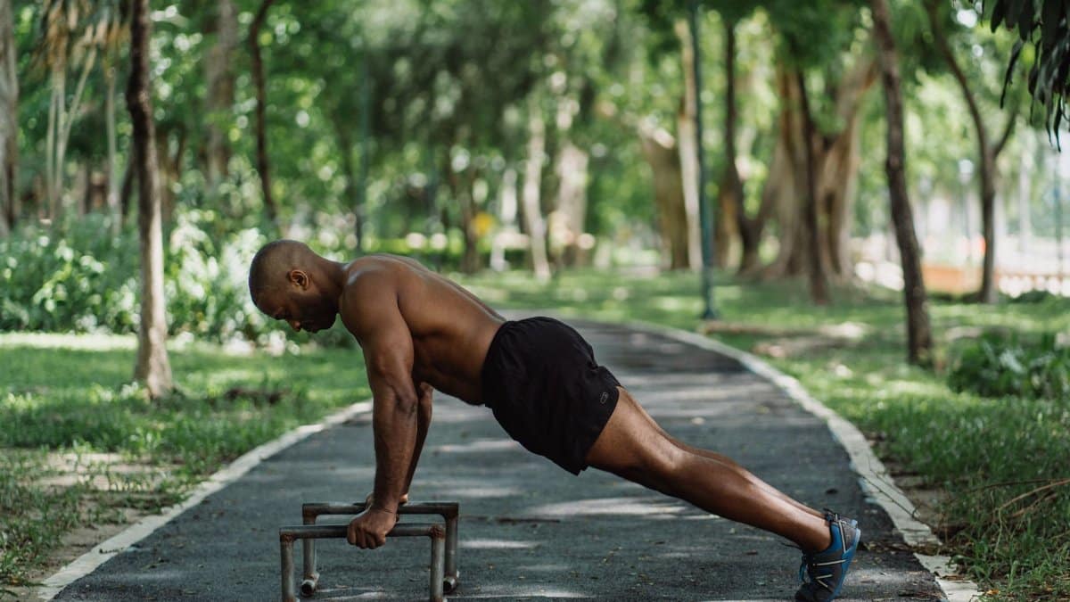 Man performing push-ups on parallel bars in a park, showcasing fitness and strength.