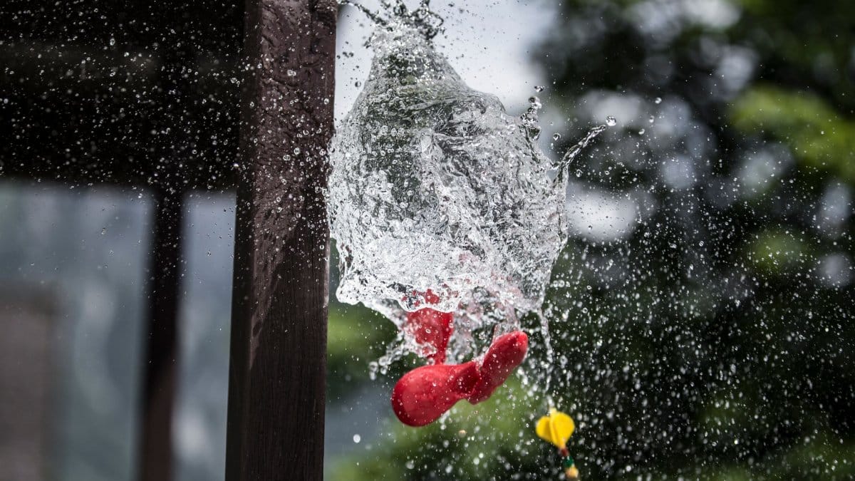 High-speed photograph capturing a water balloon burst, showing splashes and motion outdoors.