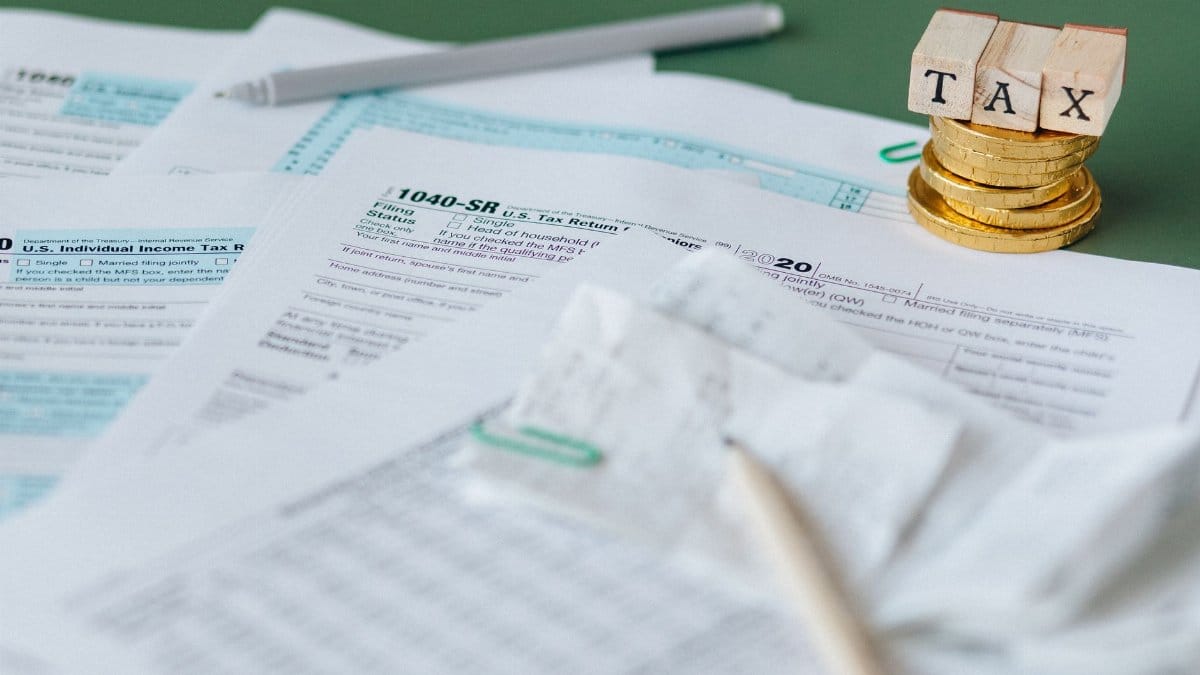 Stack of tax forms and coins with a 'TAX' stamp, symbolizing finance and accounting.