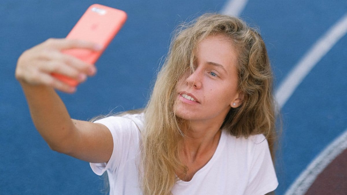 Young woman in sportswear taking selfie on mobile while sitting on sports ground in daytime
