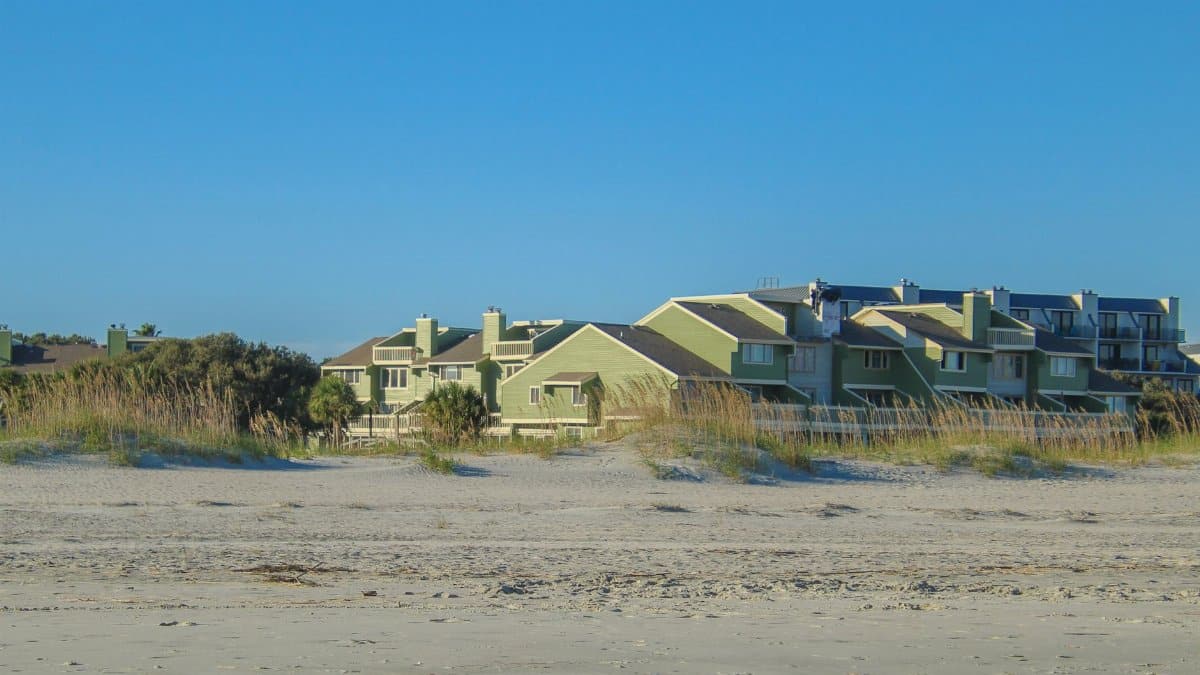 Charming beachfront condos surrounded by dune grass on a sunny day. Perfect for coastal living themes.