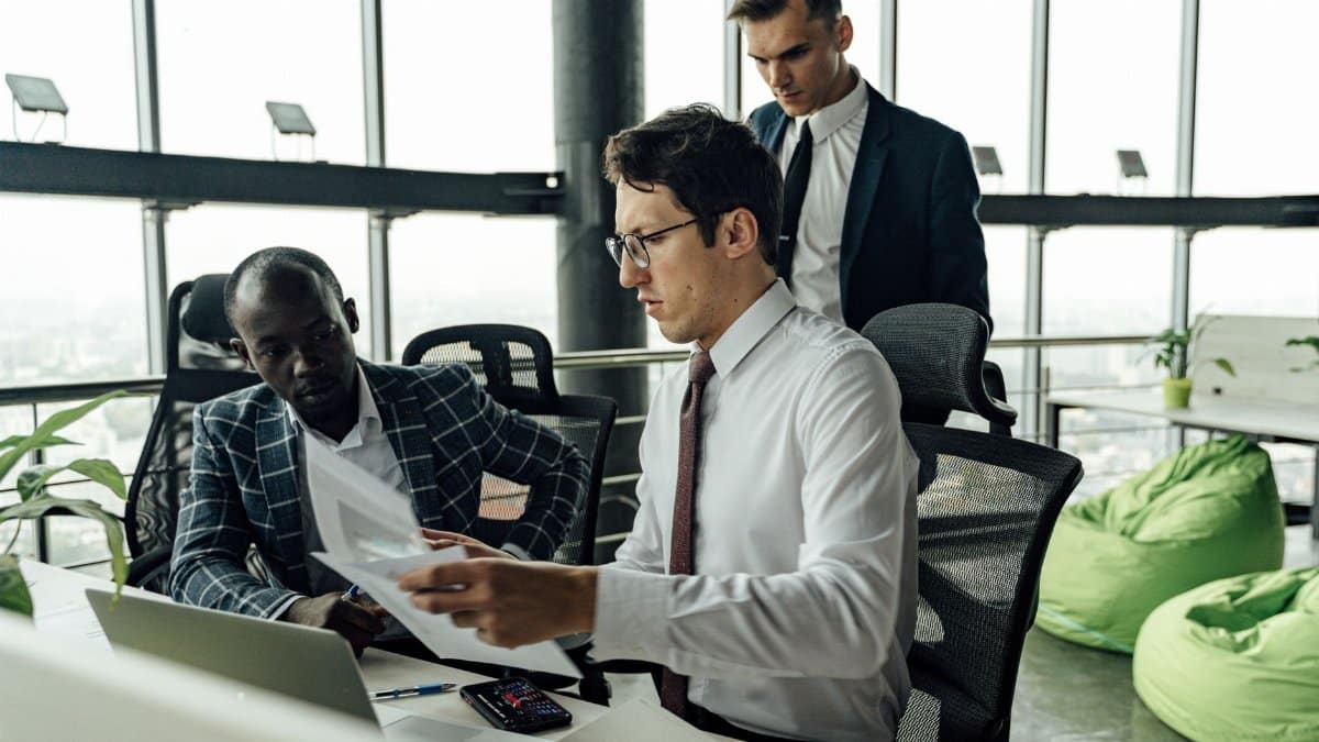 Professionals engaging in teamwork and discussion in a contemporary office setting with large windows.