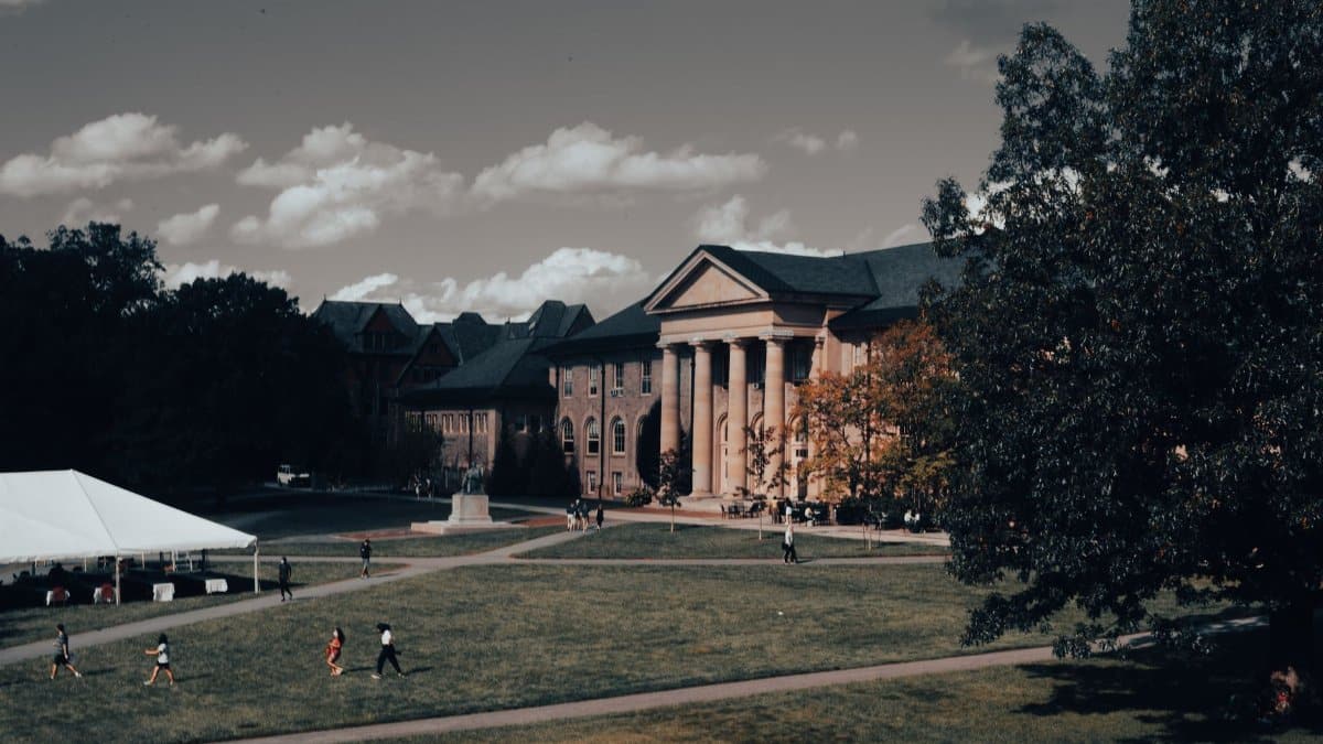 Neoclassical campus architecture with a lawn and people strolling on a sunny day.