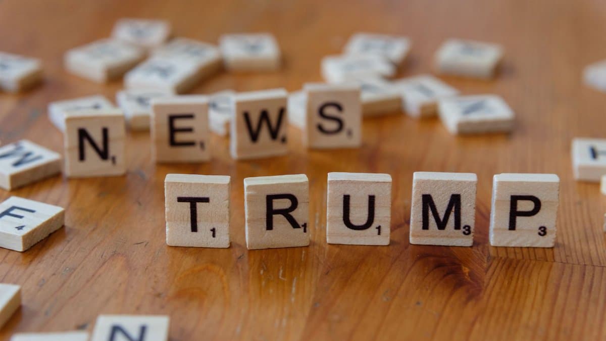 Wooden letter tiles spell 'NEWS' and 'TRUMP' on a wooden table, relating to political discourse.
