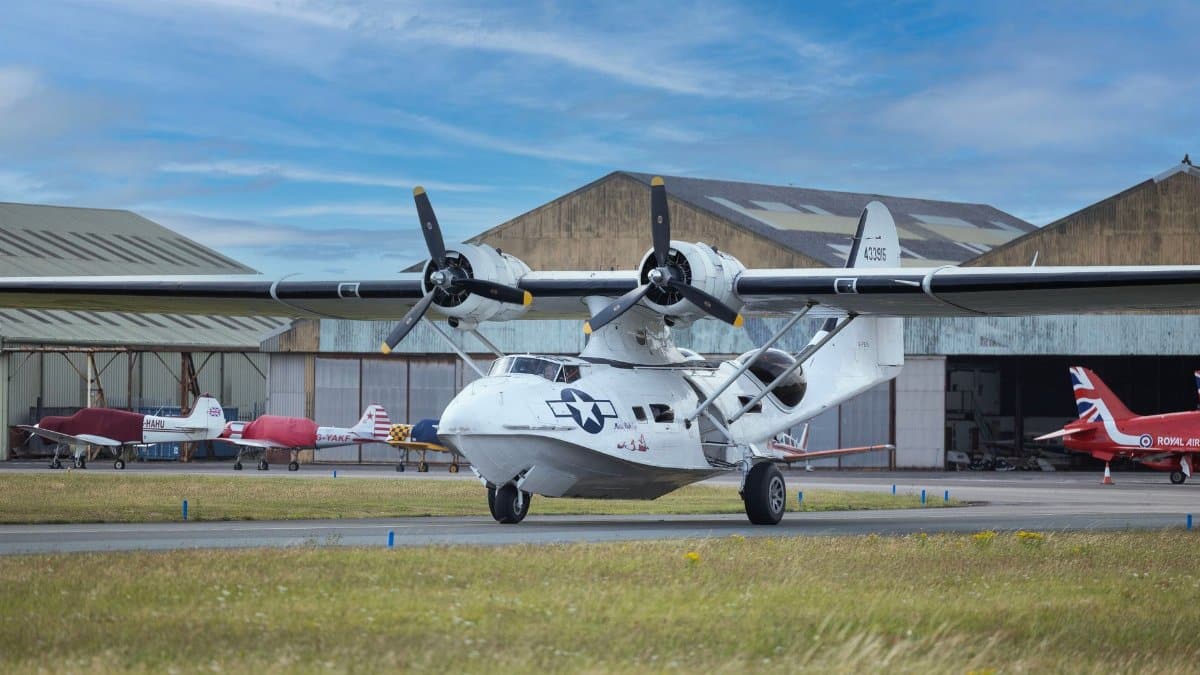 A classic aircraft parked on a runway beside an old hangar, showcasing aviation history.