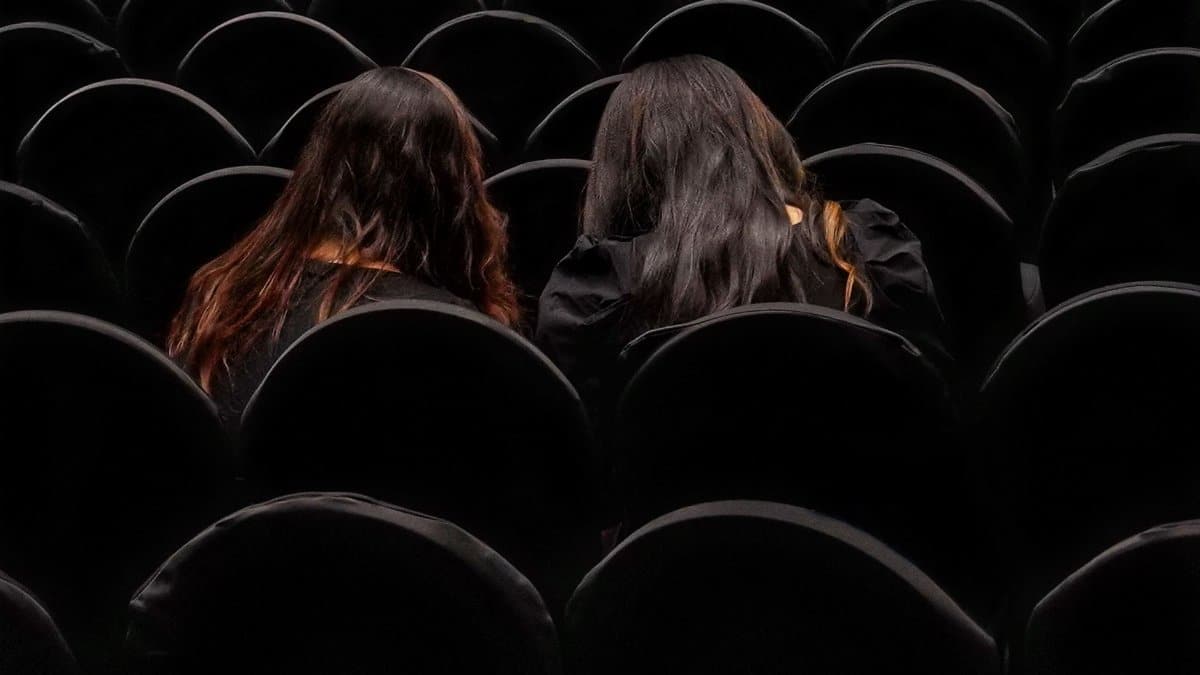 Two women seated in a dark theater, viewed from behind in Kolkata.