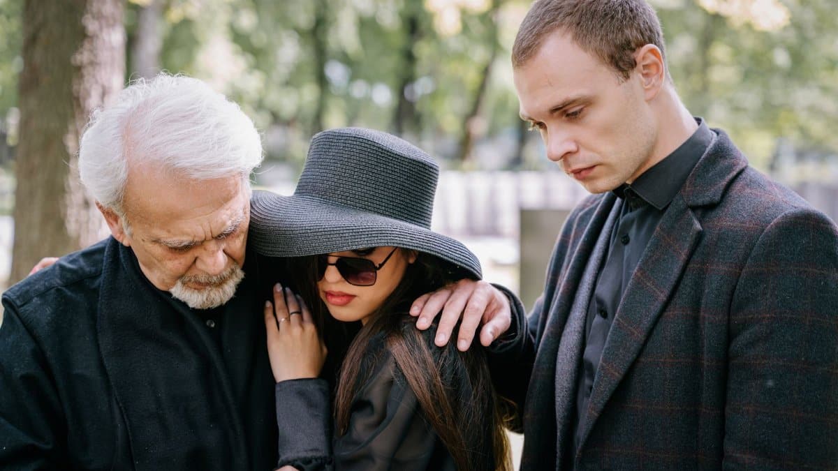 A group of adults in black clothing grieving together outdoors, conveying feelings of loss and sadness.